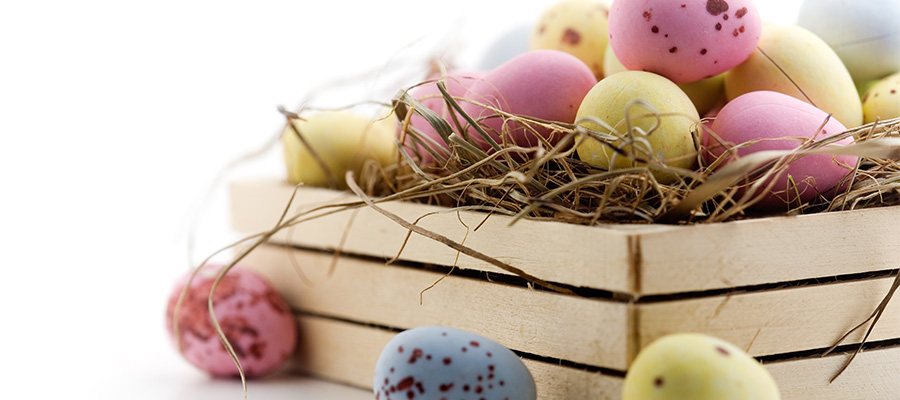 Gula, rosa och blåa små ägg placerad i och runt omkring en trälåda.