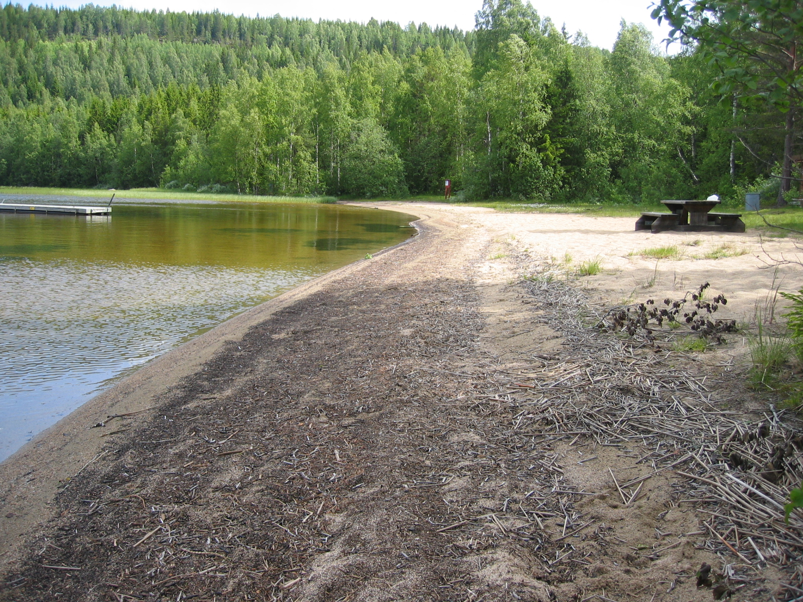 Badplats i Väster-Lövsjön, sandstrand med brygga i vattnet.