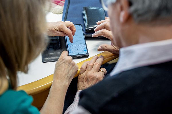 Två pensionärer tittar ner på en telefon och övar på hur man använder enheten
